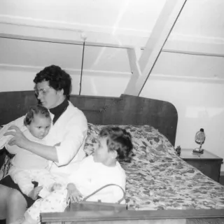 Pim Uijttewaal wordt door zijn moeder aangekleed; Karin kijkt toe en steekt haar tong uit, circa 1968.