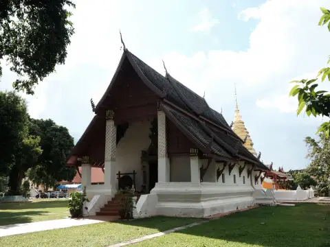 Beautiful Thai temple with traditional architecture amidst lush greenery on a sunny day.